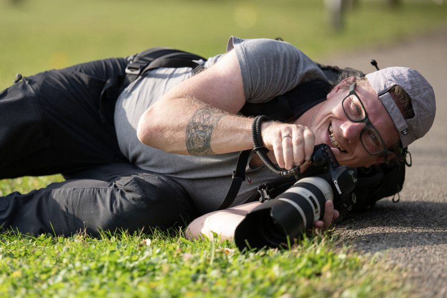 Fotograf, Tattoo, graues T-Shirt, schwarze Jeans, Brille, Mann, Wiese